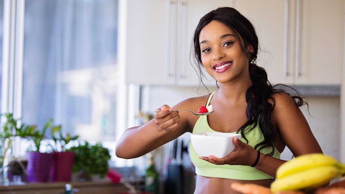 Smiling young woman in sportswear enjoying a healthy fruit snack indoors.